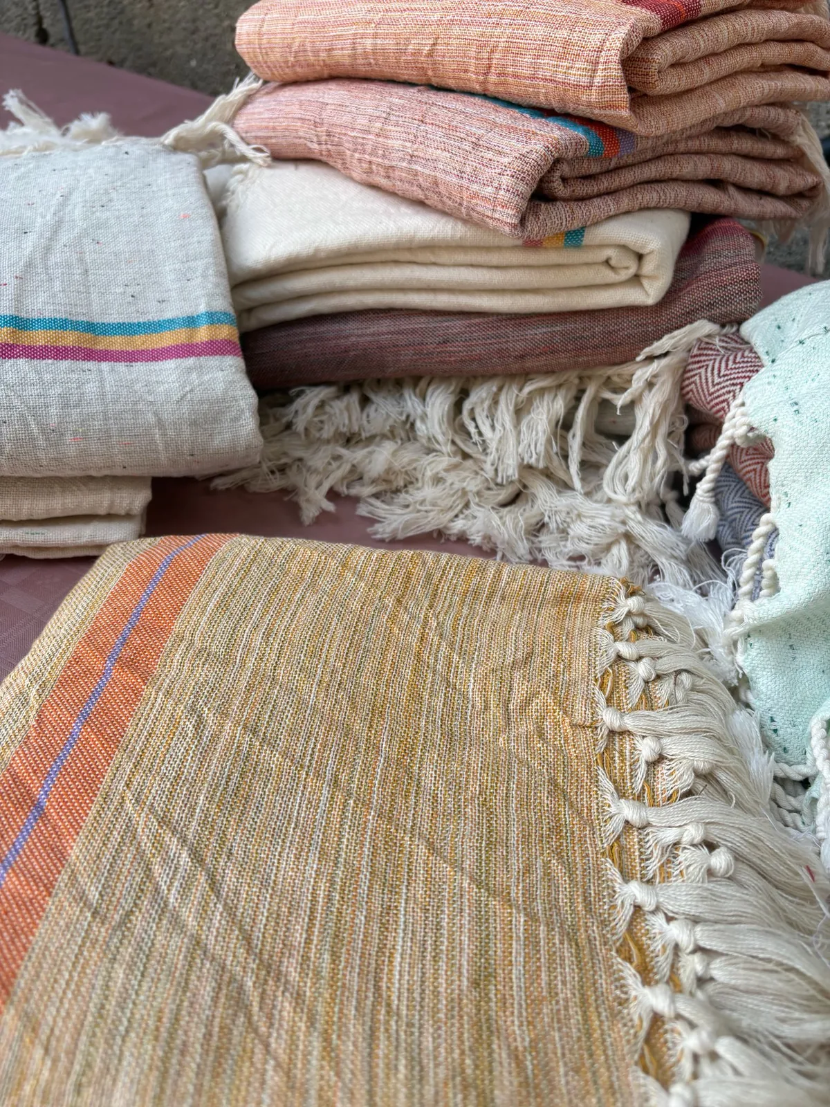 Stack of flat-woven Turkish peshtemal towels with hand-tied tassels in natural, terracotta and mint colors